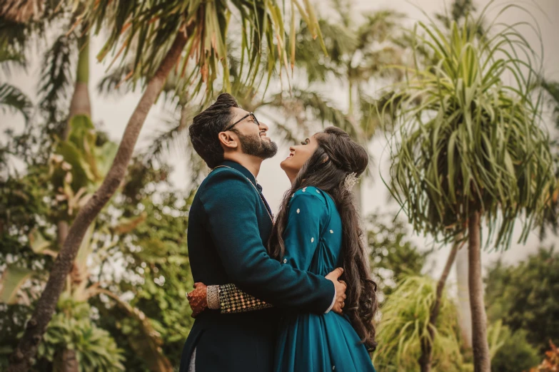 a man and woman standing next to each other in front of palm trees, pexels contest winner, hurufiyya, romantic greenery, indian, teal suit, celebrating