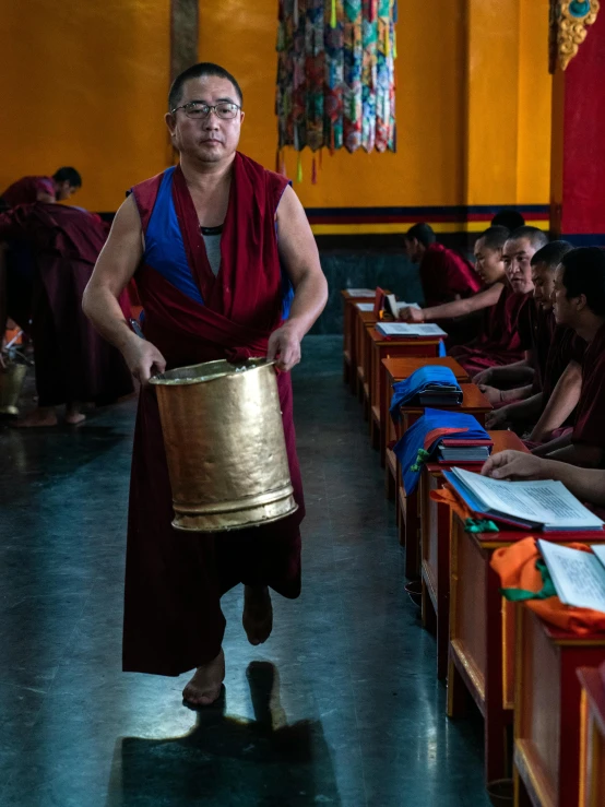 a man with a drum in a room full of people, an album cover, inspired by Steve McCurry, trending on unsplash, tibetan thangka, robed, school class, photograph 3 5 mm