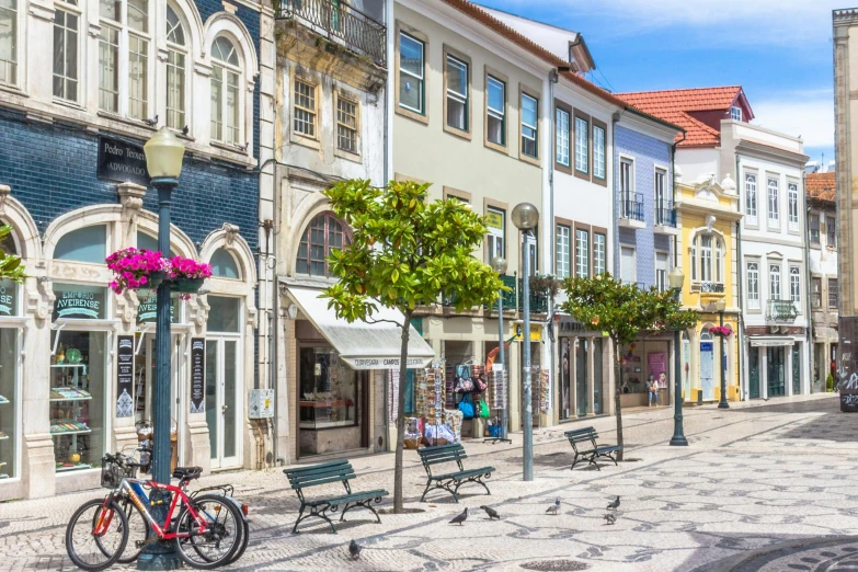 a couple of benches sitting on the side of a street, inspired by Almada Negreiros, pexels contest winner, art nouveau, square, busy small town street, tropical coastal city, preserved historical