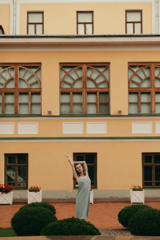 a woman standing in front of a yellow building, arabesque, doing an elegant pose over you, in russia, spa, waving