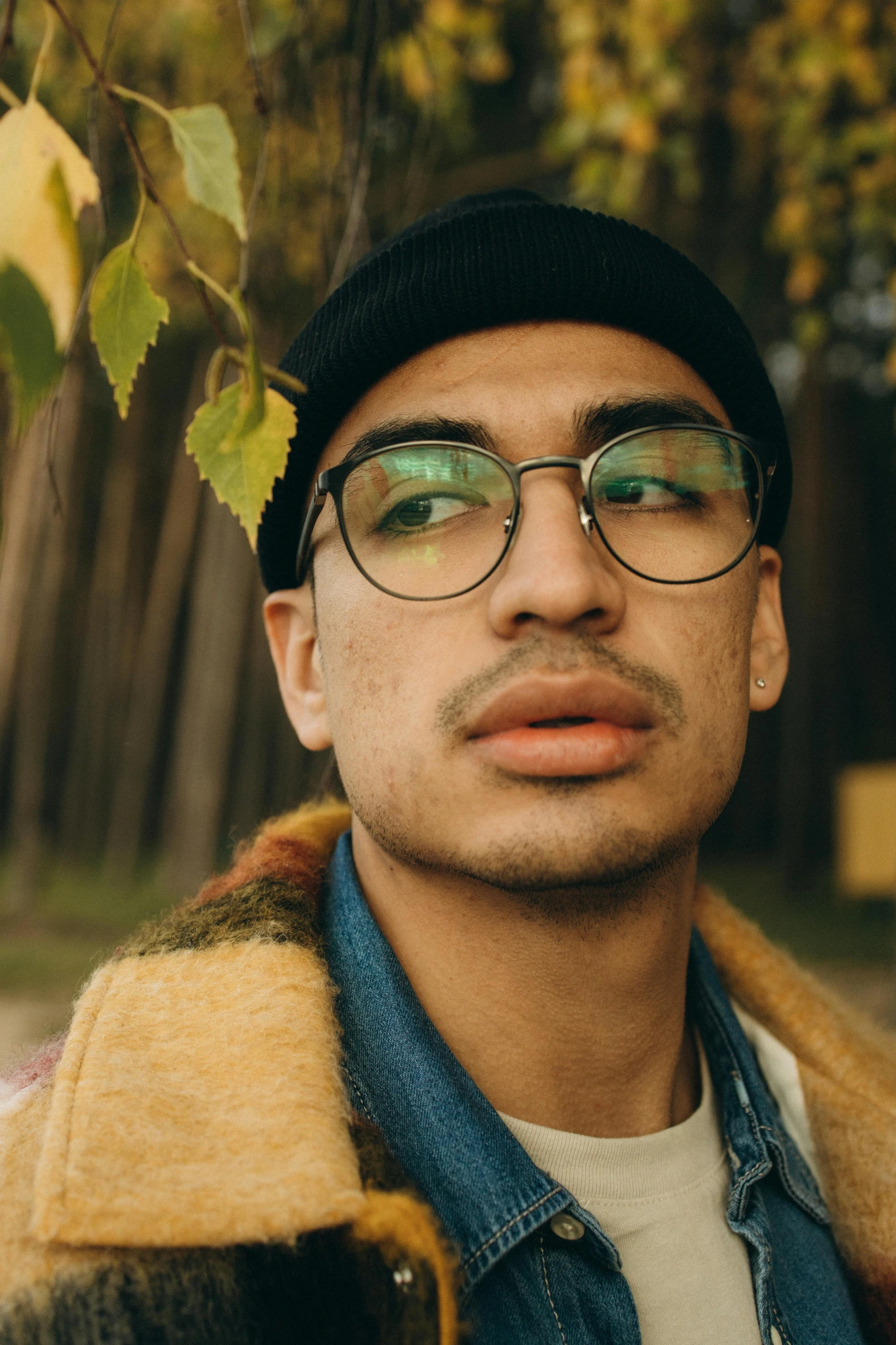 a man wearing glasses standing in front of a tree, trending on pexels, visual art, androgynous face, olive skinned, wearing teal beanie, lean man with light tan skin