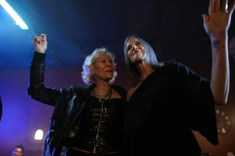 a couple of women standing next to each other on a stage, an album cover, pexels, silver haired, in a nightclub, older woman, group of people in a dark room