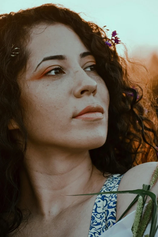 a woman with a flower in her hair, inspired by Elsa Bleda, pexels contest winner, brown curly hair, avatar image, middle eastern skin, sundown