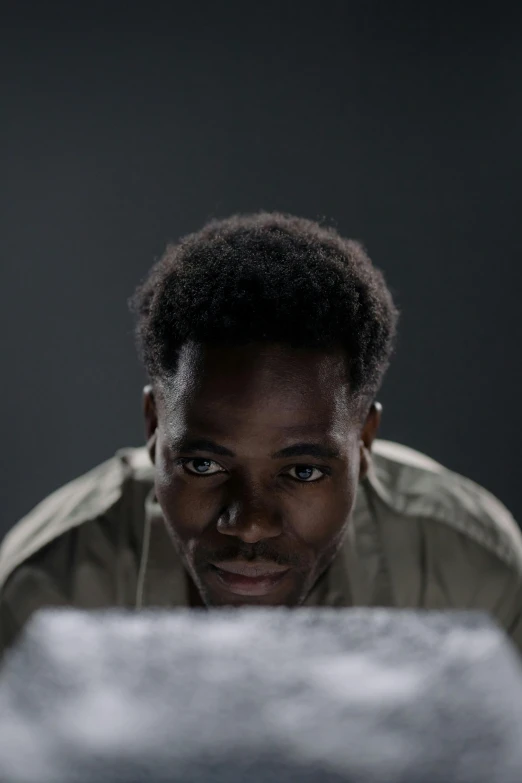 a man sitting in front of a laptop computer, a character portrait, inspired by Willian Murai, pexels contest winner, realism, darker skin, prisoner, still from a live action movie, on grey background
