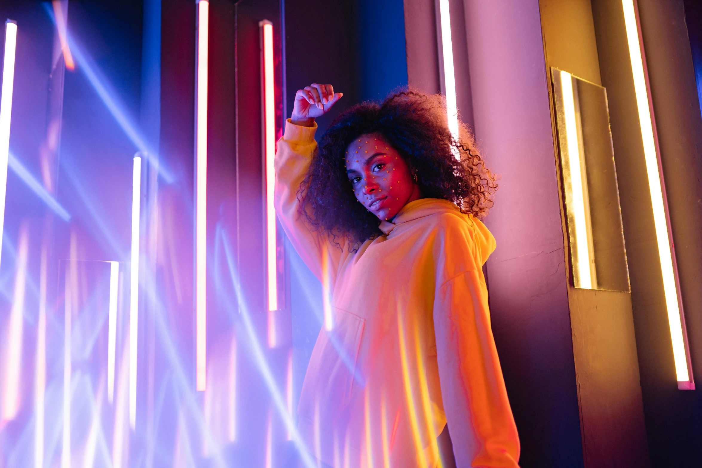 a woman standing in front of a wall with neon lights, pexels contest winner, yellow artificial lighting, imaan hammam, rainbow lighting, sza