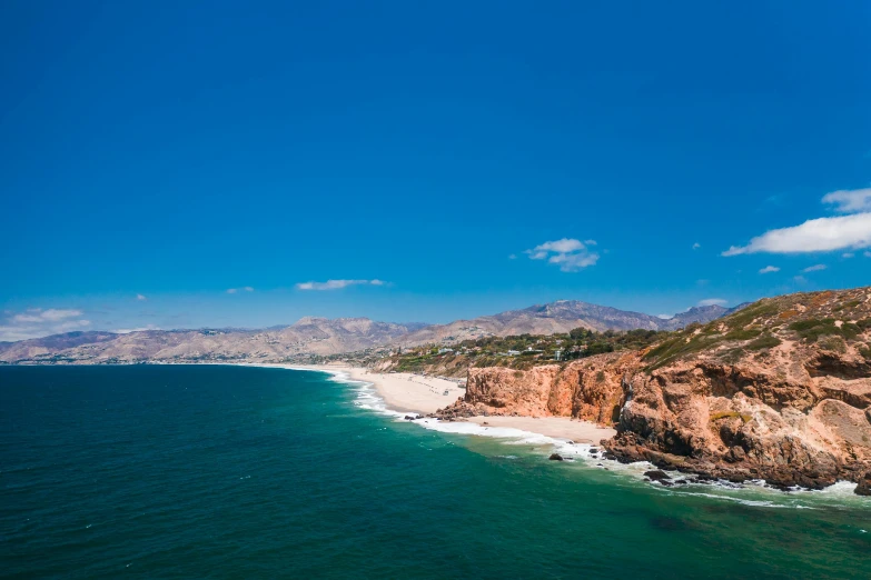 a large body of water next to a beach, pexels contest winner, renaissance, malibu canyon, blue clear skies, beach is between the two valleys, conde nast traveler photo