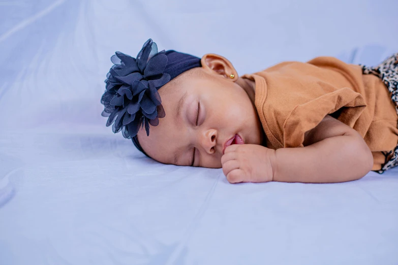 a close up of a baby sleeping on a bed, navy, girl with a flower head, navy blue, mixed race