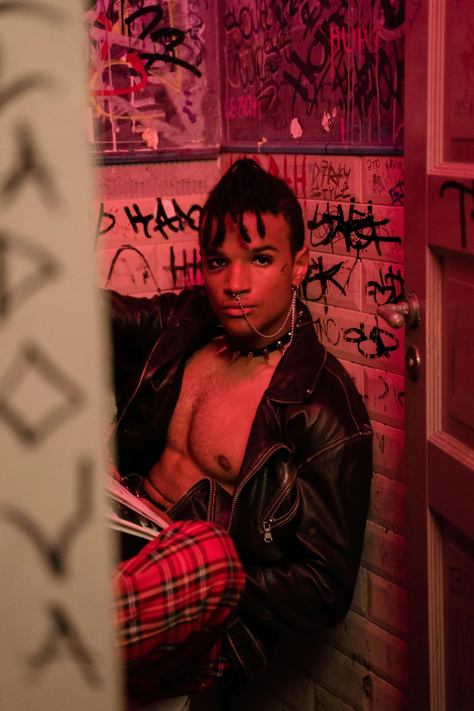 a man in a room with graffiti on the walls, an album cover, inspired by Nan Goldin, trending on pexels, in a leather corset, xxxtentacion, non binary model, giddy smirk