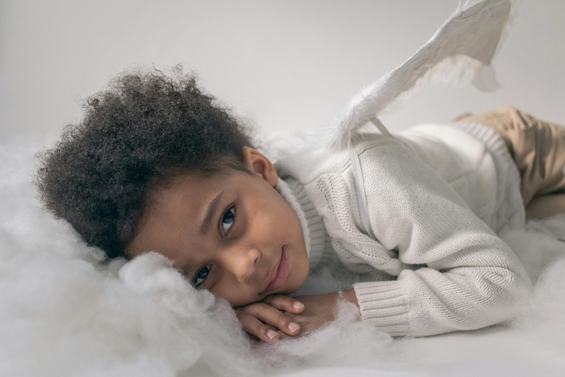 a close up of a child laying on a cloud, inspired by Sophie Anderson, pexels contest winner, black angel wings, photoshoot for skincare brand, wearing a white sweater, full - body majestic angel