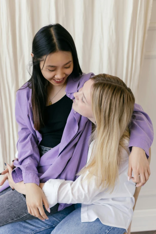 a couple of women sitting next to each other, a picture, inspired by Ruth Jên, trending on pexels, purple jacket, embracing, wearing lab coat and a blouse, young asian woman