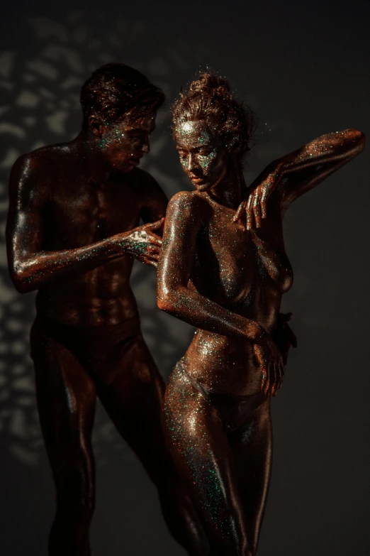 a man and a woman standing next to each other, a bronze sculpture, inspired by Hans Erni, pexels contest winner, figurative art, body painted with black fluid, chocolate art, bathing in light, female model