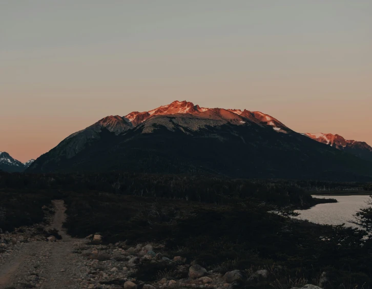 a dirt road next to a body of water with a mountain in the background, an album cover, unsplash contest winner, last light on mountain top, whistler, expansive view, background : diego fazio