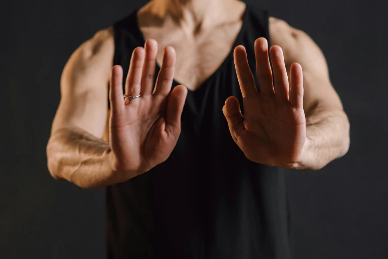 a man that is standing up with his hands in the air, wearing a cropped black tank top, close-up of thin soft hand, martial art pose, background image
