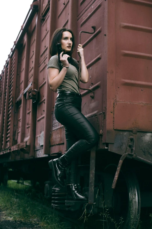 a woman talking on a cell phone next to a train, an album cover, by Lucia Peka, pexels contest winner, leather pants, military clothing, better known as amouranth, full body action pose