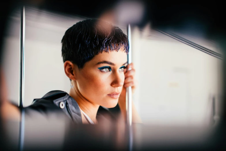 a woman looking at herself in a mirror, an album cover, trending on pexels, photorealism, short black pixie cut hair, bokeh + dof + 8k, neon blue highlights, fashion model portrait