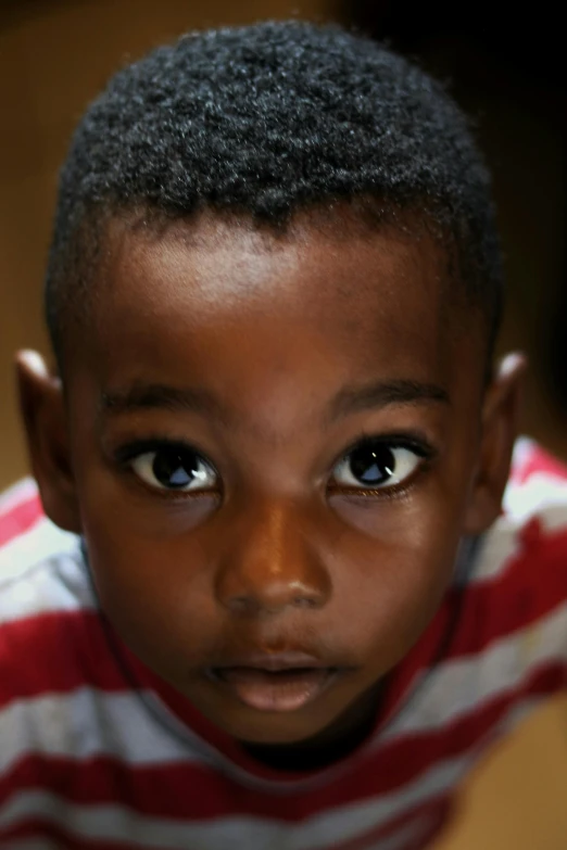 a young boy wearing a red and white striped shirt, an album cover, pexels contest winner, hurufiyya, african facial features, curious eyes, ( ( dark skin ) ), high angle closeup portrait