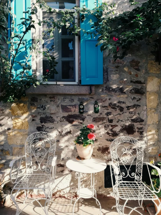 a couple of chairs sitting on top of a patio, blue shutters on windows, entwined in vines and nature, morning coffee, greek setting