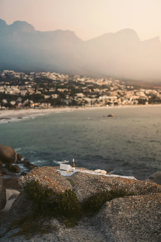 a teddy bear sitting on top of a rock next to the ocean, whitewashed buildings, at the golden hour, birds - eye view, lush surroundings