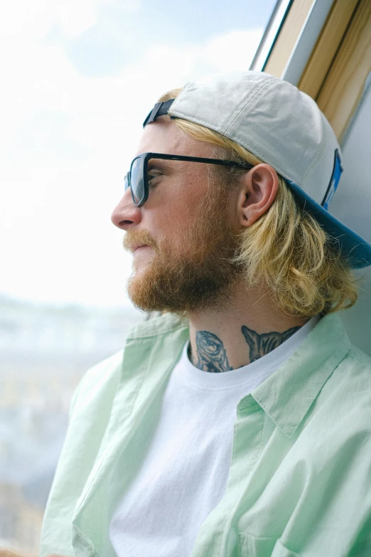 a man wearing a hat and sunglasses looking out a window, a tattoo, trending on pexels, blond beard, mullet haircut, an ocean, mac miller