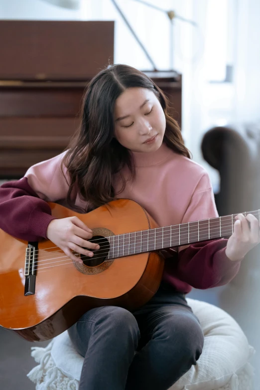 a woman sitting on a couch playing a guitar, inspired by Gu Kaizhi, pexels contest winner, li bingbing, yanjun chengt, ( ( theatrical ) ), black haired girl wearing hoodie