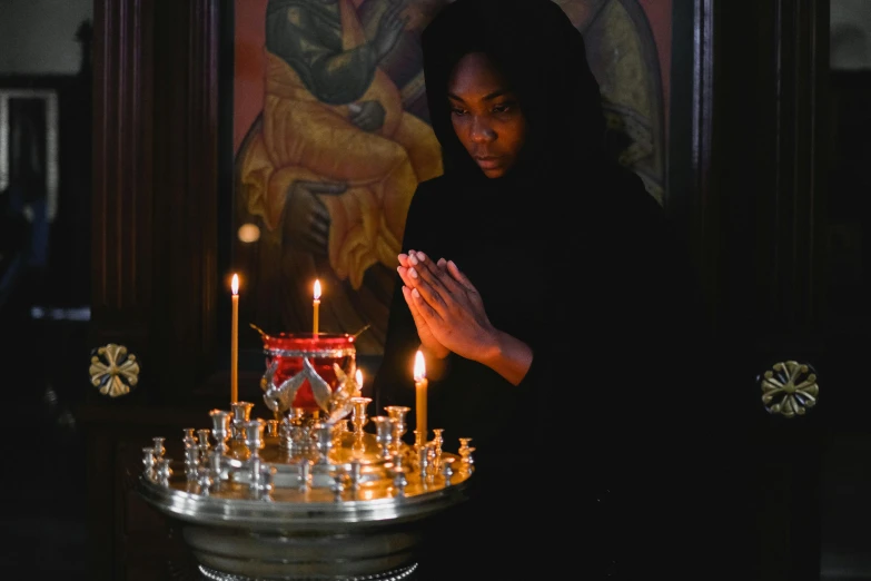 a woman lighting a candle in a church, pexels contest winner, aida muluneh, wearing a black robe, orthodox icons, riyahd cassiem