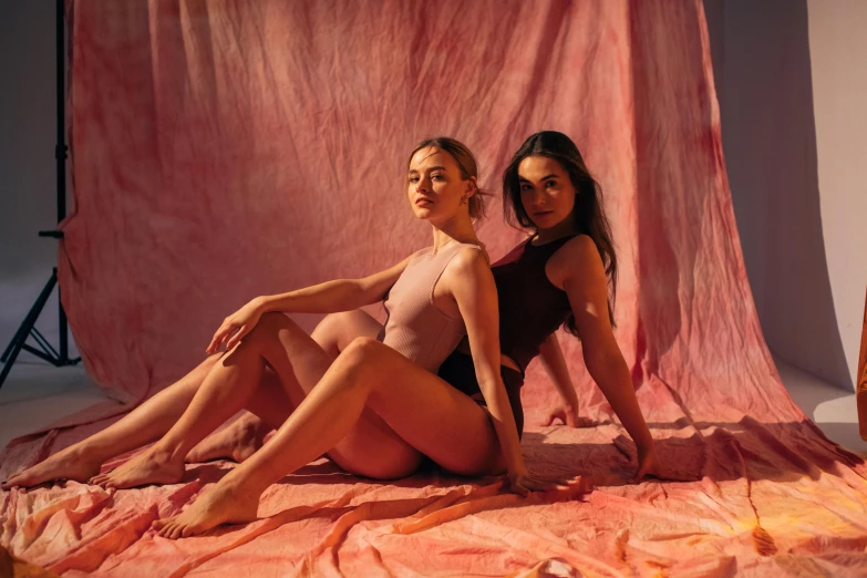 a couple of women sitting on top of a pink blanket, a portrait, by Lee Loughridge, pexels contest winner, leotard, tan skin, bella poarch, photoshoot for skincare brand