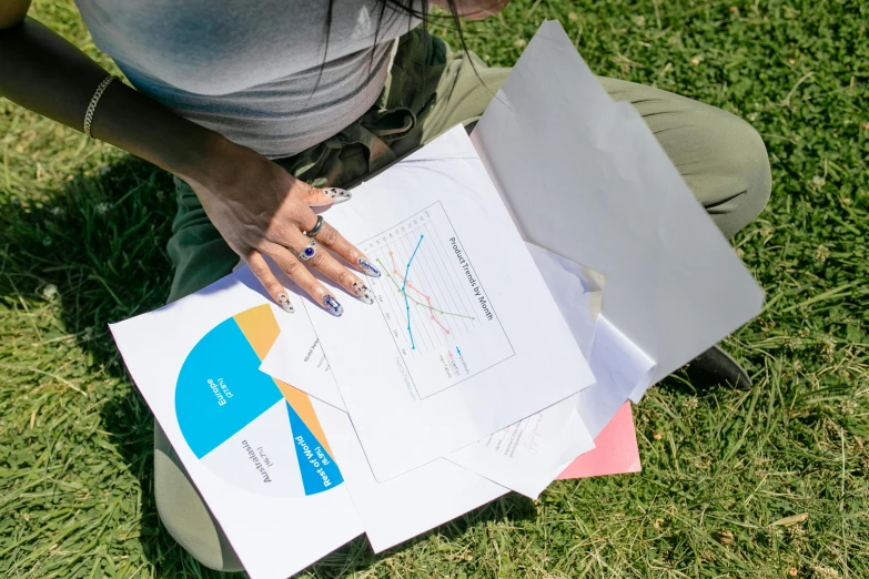 a woman sitting on the ground holding a piece of paper, unsplash, informative graphs and diagrams, sydney park, thumbnail, lawn