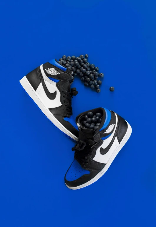 a pair of black and white sneakers on a blue background, an album cover, by Paul Bird, trending on unsplash, photorealism, wearing a blue berries, air jordan 1 high, dark blue spheres fly around, juice