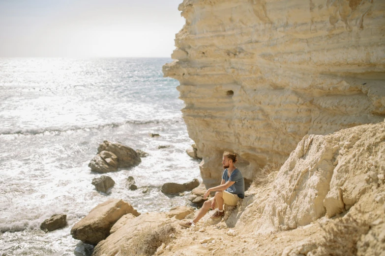 a man sitting on top of a rock next to the ocean, over a chalk cliff, profile image, cyprus, australian beach