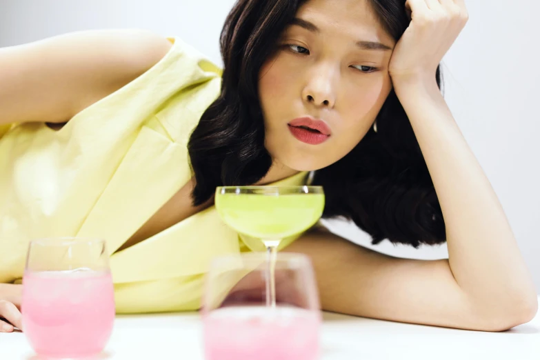 a woman sitting at a table with a glass of pink liquid in front of her, inspired by Fei Danxu, trending on pexels, renaissance, looking exhausted, draped in fleshy green and pink, asian descent, people drink cocktails