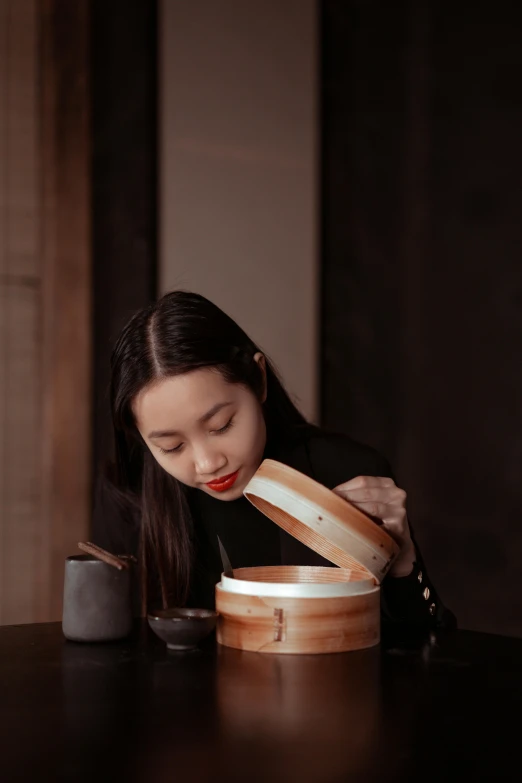 a woman sitting at a table eating a sandwich, a picture, inspired by Qian Du, pexels contest winner, mingei, wooden bowl, box, profile image, lacquerware