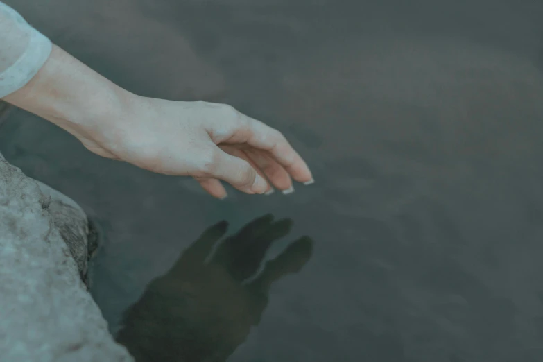 a person standing on top of a rock next to a body of water, inspired by Elsa Bleda, pexels contest winner, realism, close-up of thin soft hand, a pale skin, [ floating ]!!, in muted colours