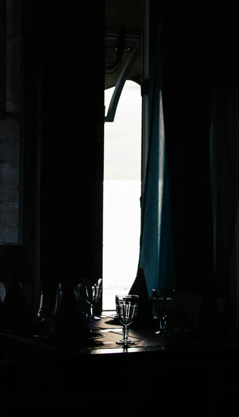 a couple of wine glasses sitting on top of a table, by Elsa Bleda, open door, silhouetted, curtain, inside a tavern