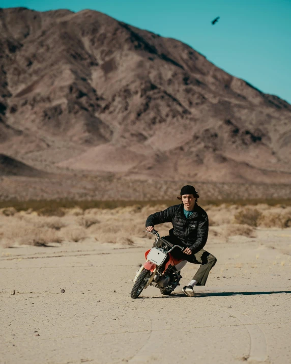 a man riding on the back of a motorcycle in the desert, a colorized photo, by Kyle Lambert, unsplash contest winner, finn wolfhard, mid-shot of a hunky, wheelie, david marquez