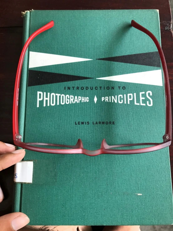 a person holding a book with a pair of glasses on it, an album cover, by Ben Zoeller, unsplash, 1950s photograph, shot with iphone 1 0, national geographic photograph, display item