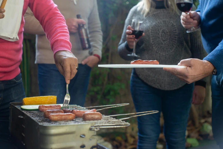 a group of people standing around a grill with hot dogs on it, pexels contest winner, wine, using fork, profile image, back towards camera