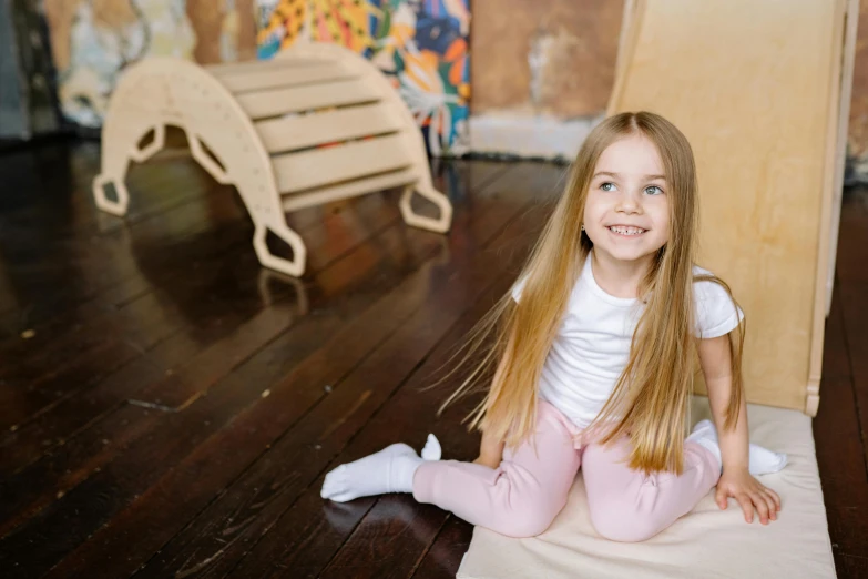 a little girl sitting on top of a wooden floor, posing for a picture