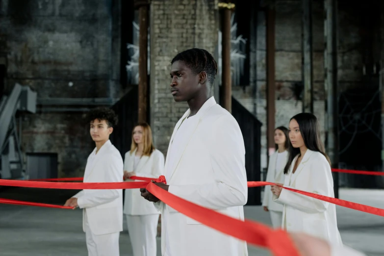 a group of people standing around a red ribbon, inspired by Vanessa Beecroft, pexels contest winner, gutai group, a black man with long curly hair, wearing futuristic white suit, standing in front of the altar, [ theatrical ]