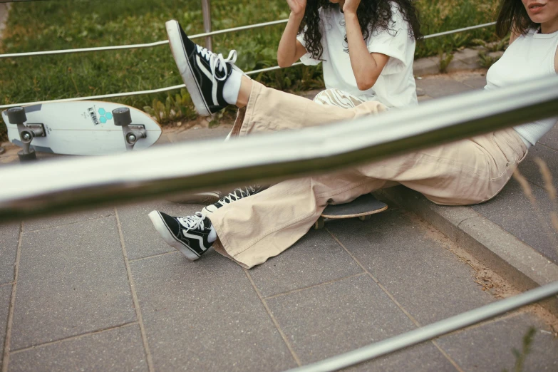 two women sitting on the ground talking on their cell phones, by Emma Andijewska, trending on pexels, realism, detailed skateboard, uniform off - white sky, on a table, curled perspective