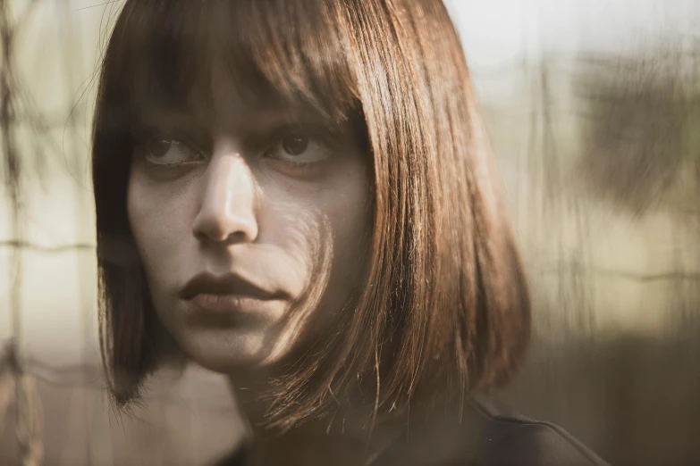 a close up of a person near a fence, an album cover, inspired by Elsa Bleda, pexels contest winner, chrome bob haircut, brown hair fringe, looking in mirror, haunting beautiful young woman