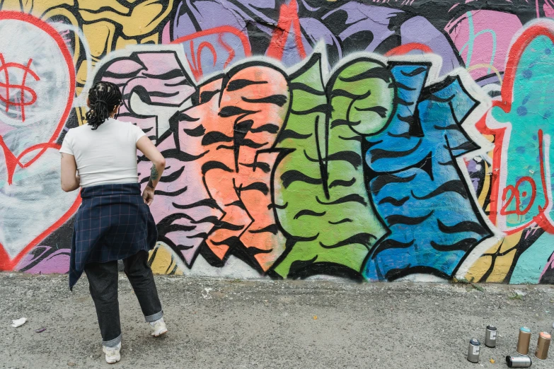 a woman standing in front of a wall covered in graffiti, graffiti art, facing away from the camera, multicoloured, filling the frame, a person standing in front of a
