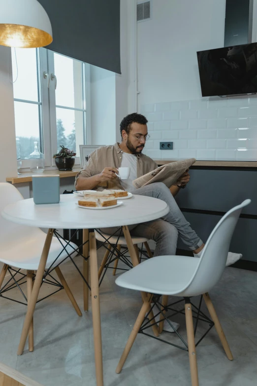 a man sitting at a table reading a book, pexels contest winner, white kitchen table, having a snack, sleek design, low quality photo