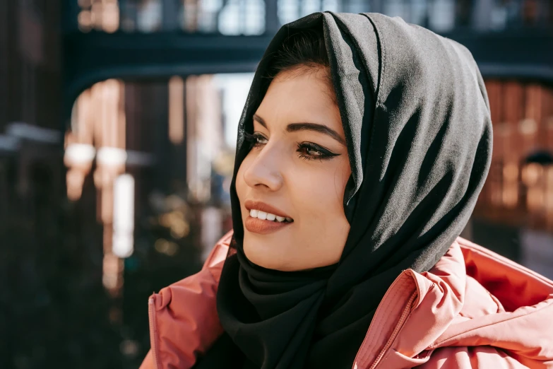 a woman wearing a pink jacket and a black scarf, inspired by Maryam Hashemi, trending on pexels, hurufiyya, middle eastern skin, black, malaysian, sunny day time