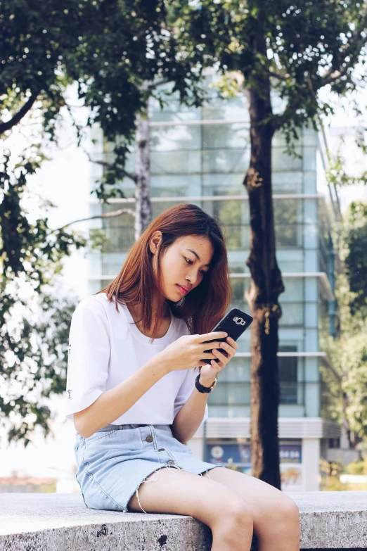 a woman sitting on a ledge looking at her cell phone, a cartoon, trending on pexels, vietnamese woman, square, dressed in a white t shirt, 33mm photo