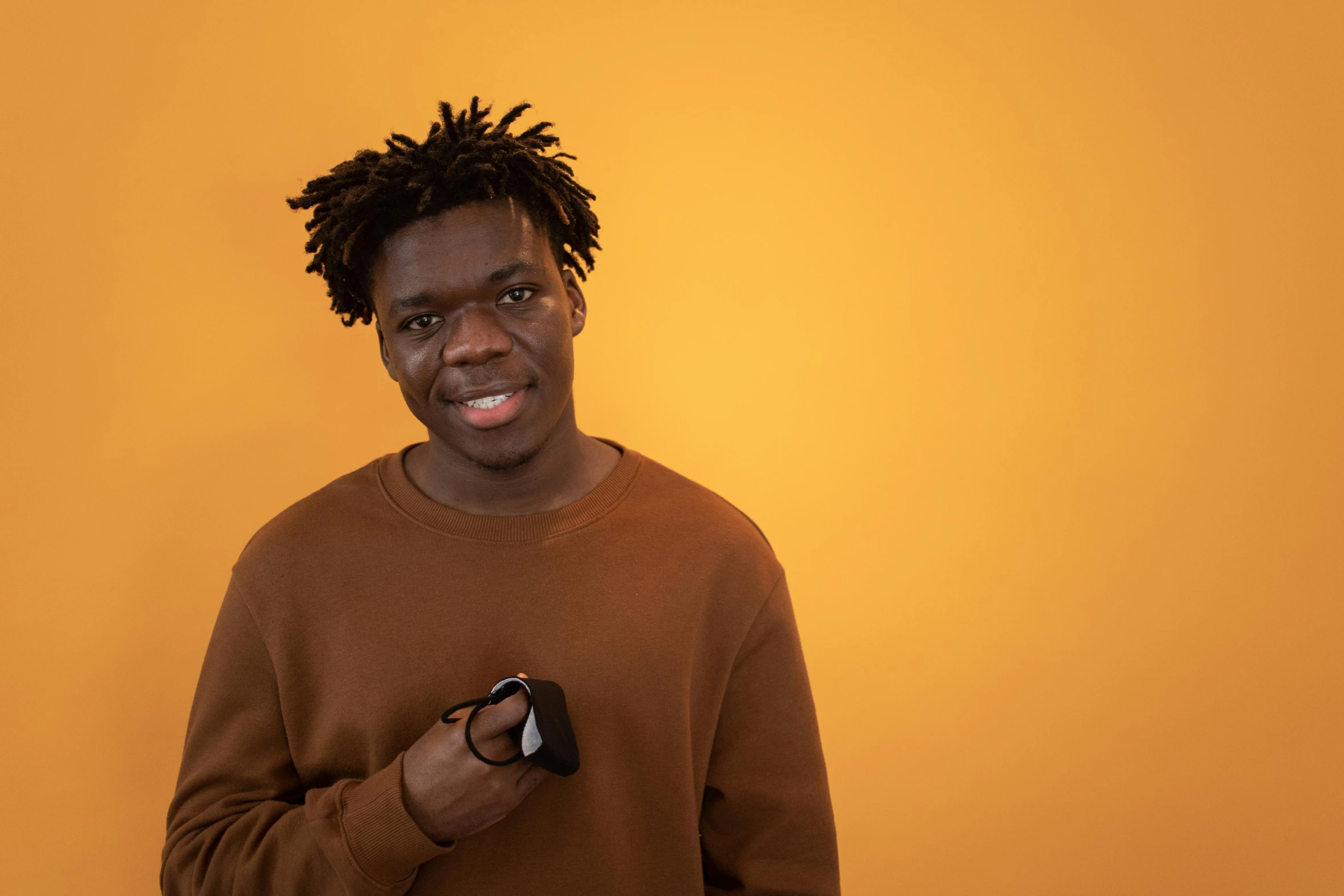 a man with dreadlocks holding a remote control, pexels contest winner, hurufiyya, in front of an orange background, he is wearing a brown sweater, he is about 20 years old | short, headshot profile picture