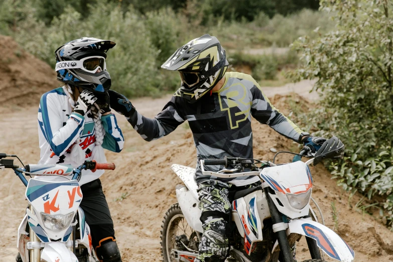 a couple of men standing next to each other on dirt bikes, a picture, unsplash, figuration libre, avatar image, close-up photo, reaching out to each other, sports clothing