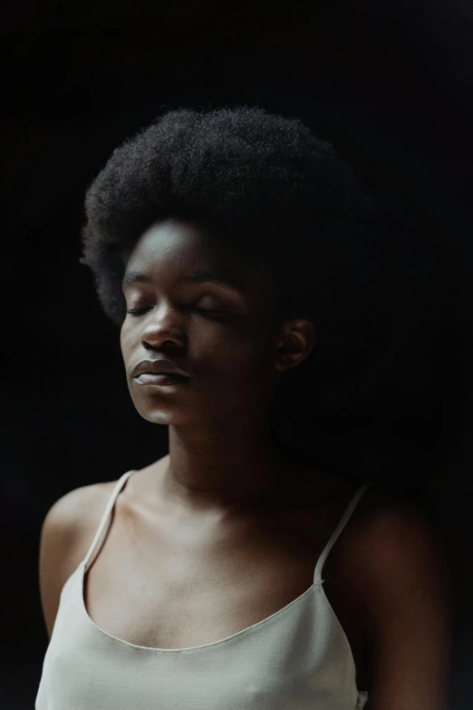 a woman standing in front of a black background, by Lily Delissa Joseph, pexels contest winner, afrofuturism, soft shadows, fashion model face closed eyes, natural hair, studio medium format photograph