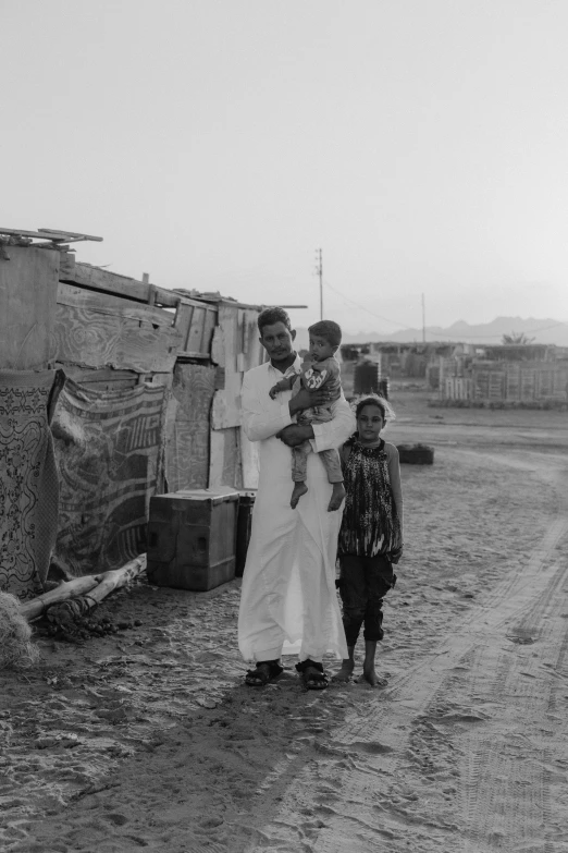 a black and white photo of a woman holding a child, a black and white photo, by Youssef Howayek, dada, shanty townships, man standing, medium format. soft light, oman