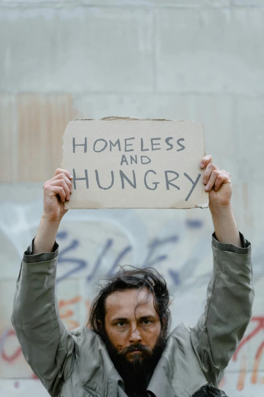 a man holding a sign that says homeless and hungry, an album cover, by Matija Jama, trending on unsplash, renaissance, timothee chalamet, square, sustainability, frank dillane