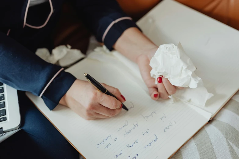 a woman sitting on a couch writing on a piece of paper, by Julia Pishtar, pexels contest winner, cream paper, background image, miscellaneous objects, professional image